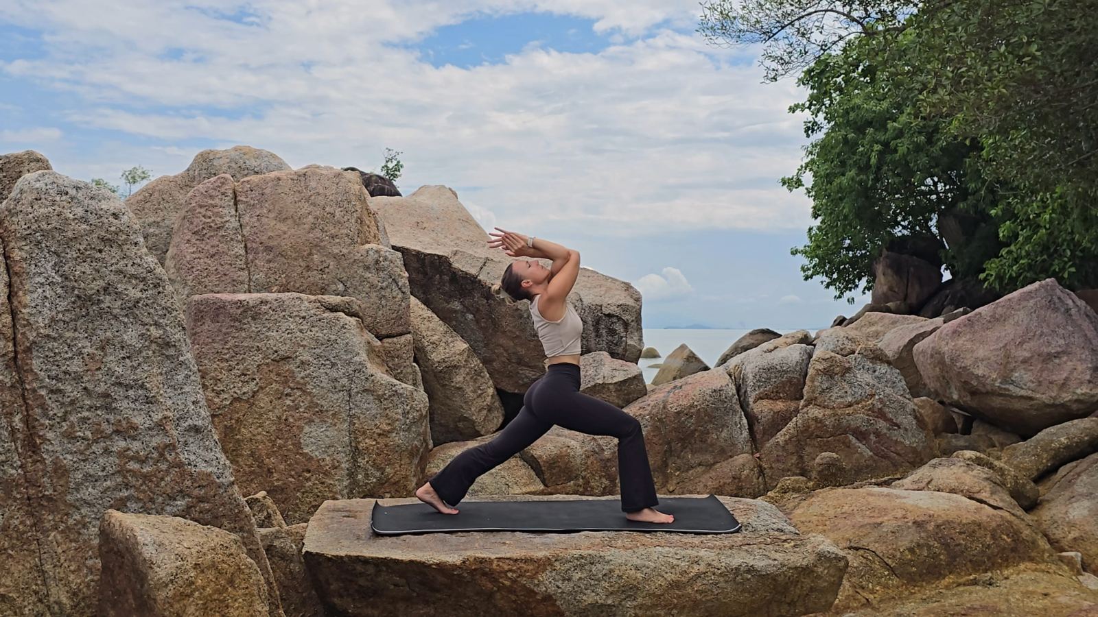 Jen practicing a warrior pose on coastal rocks