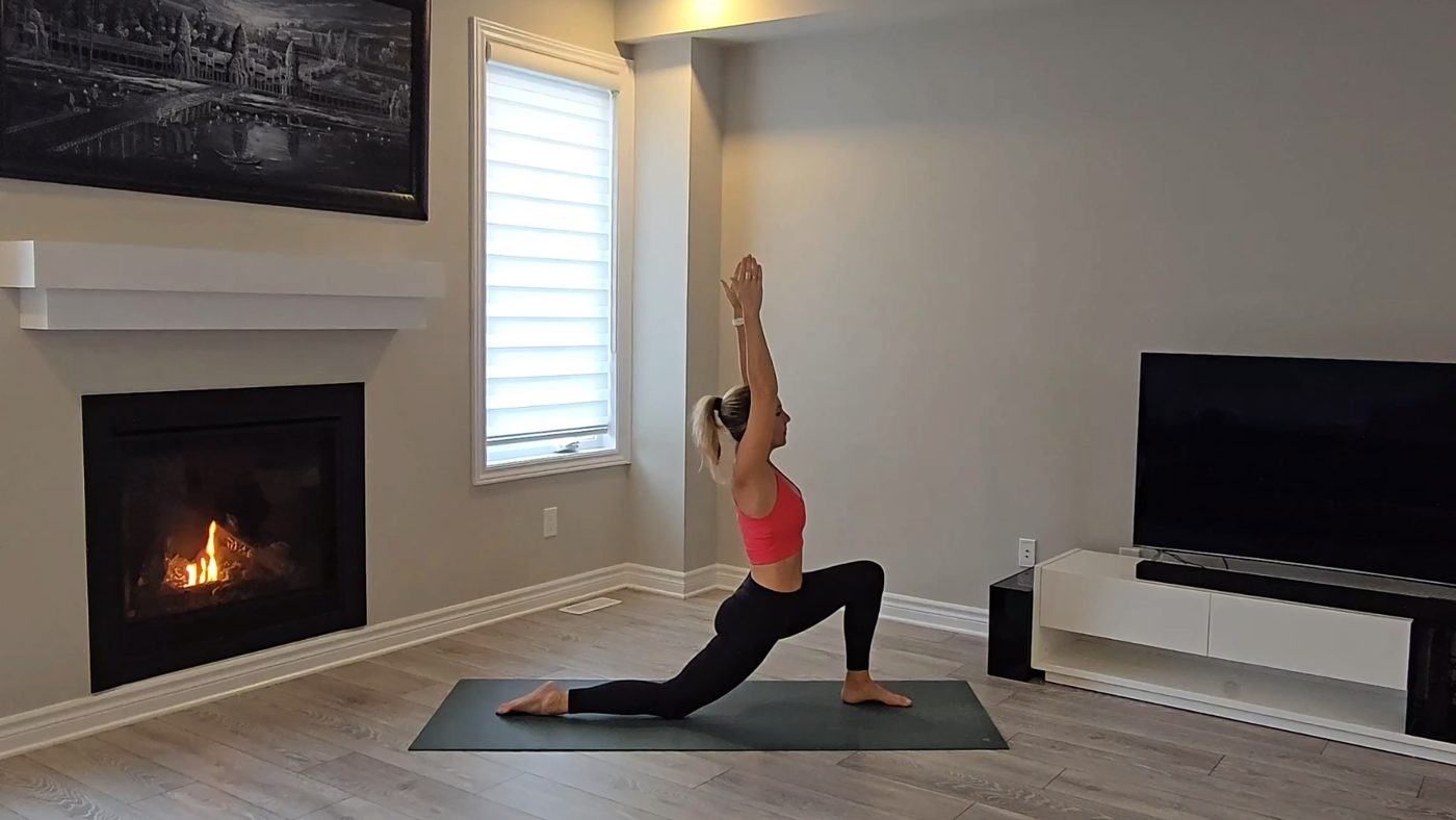 Jen in a deep Crescent Lunge with arms raised by a fireplace