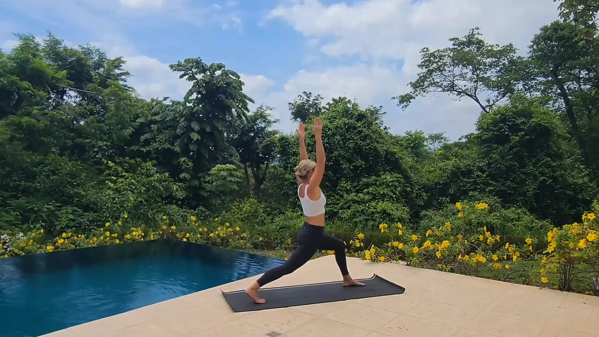Jen in Crescent Lunge with arms raised in an ocean view gazebo